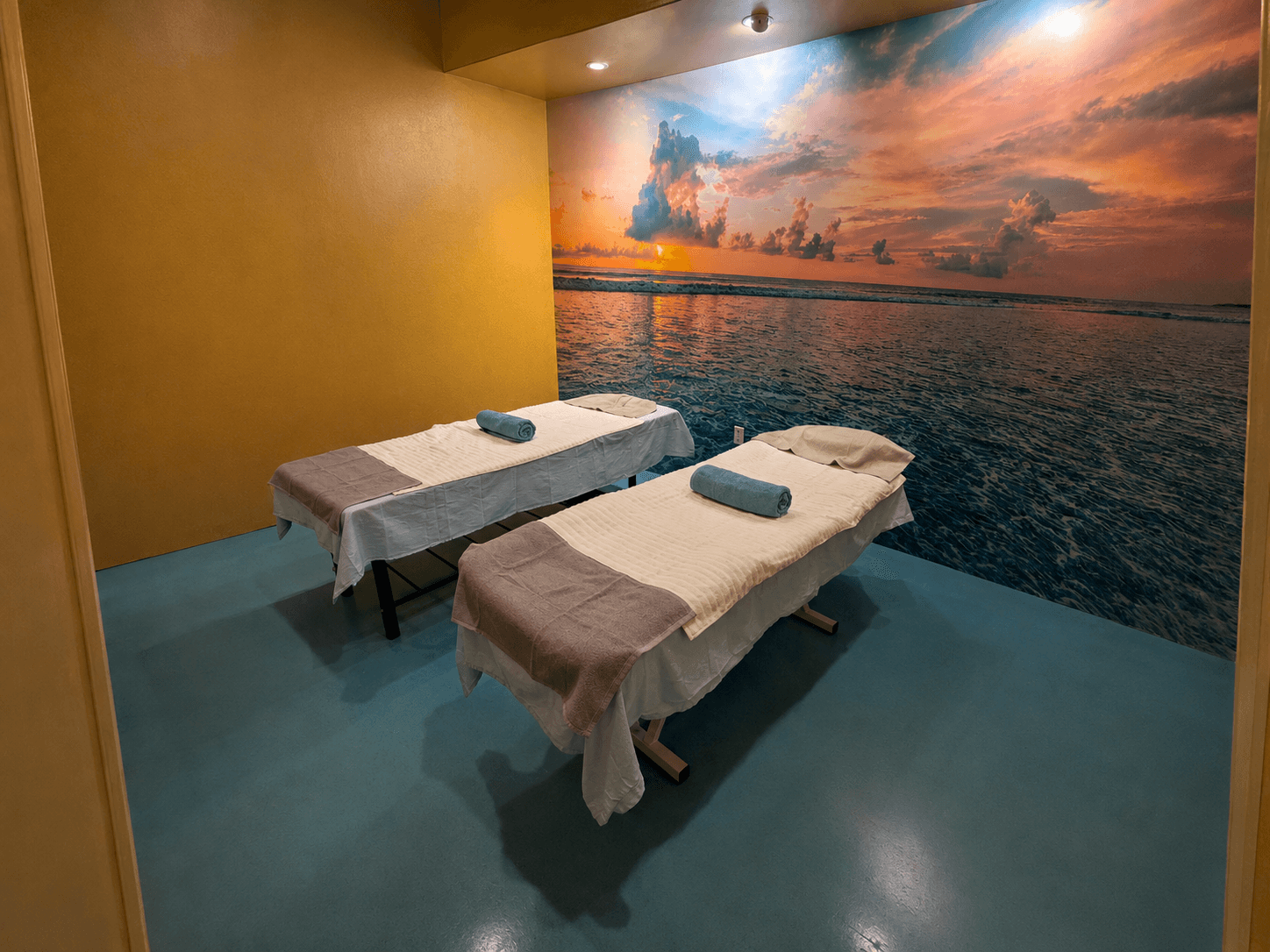 Habitación para masaje en pareja con dos camillas preparadas, toallas limpias y un mural del océano al atardecer en Masaje Milagroso Dávila, Tijuana.