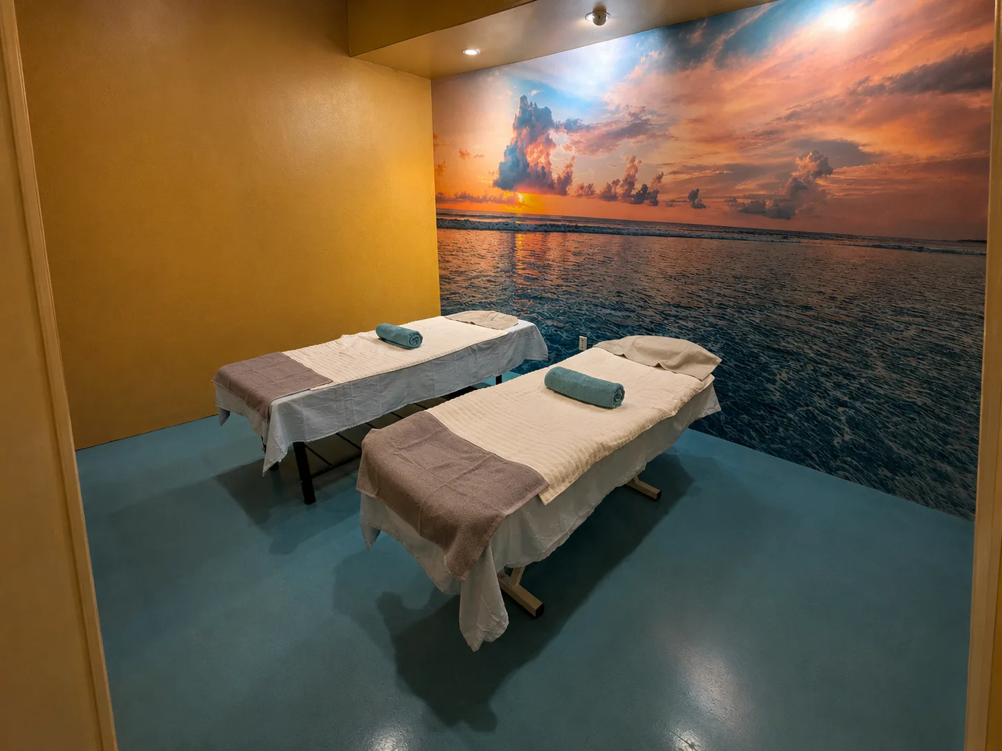 Habitación para masaje en pareja con dos camillas preparadas, toallas limpias y un mural del océano al atardecer en Masaje Milagroso Dávila, Tijuana.